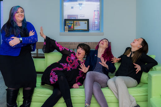 A group of four women energetically interacting and laughing on a green couch, illustrating vitality and joy relevant to Tongkat Ali's benefits.